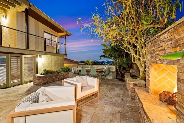 patio terrace at dusk featuring a balcony, an outdoor stone fireplace, and outdoor dining area