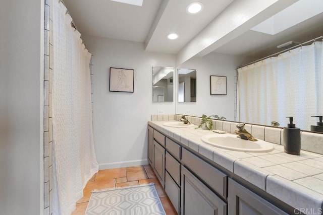 full bathroom featuring double vanity, a skylight, baseboards, and a sink