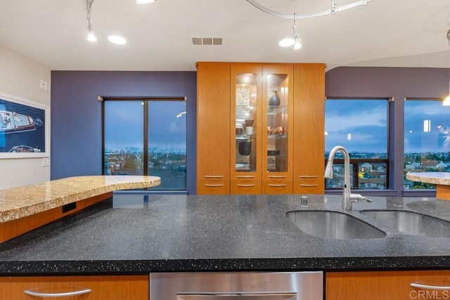 kitchen featuring visible vents, brown cabinetry, dishwasher, dark stone countertops, and a sink