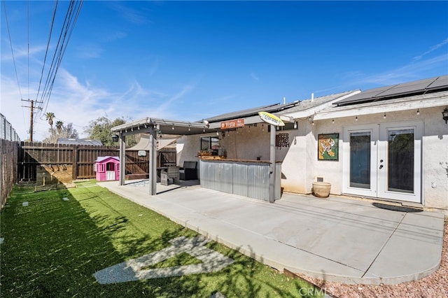 rear view of property with french doors, stucco siding, roof mounted solar panels, a patio area, and a fenced backyard