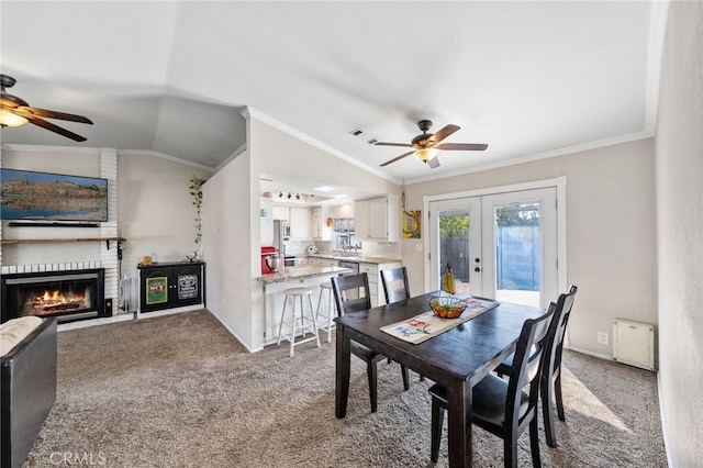 carpeted dining area featuring french doors, crown molding, a brick fireplace, vaulted ceiling, and ceiling fan