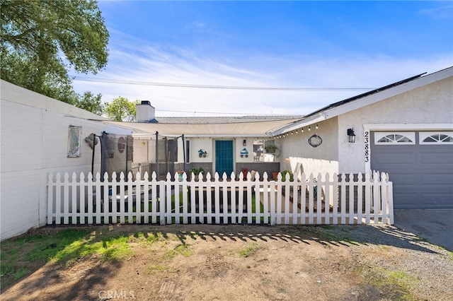 ranch-style home with a fenced front yard, a chimney, an attached garage, and stucco siding