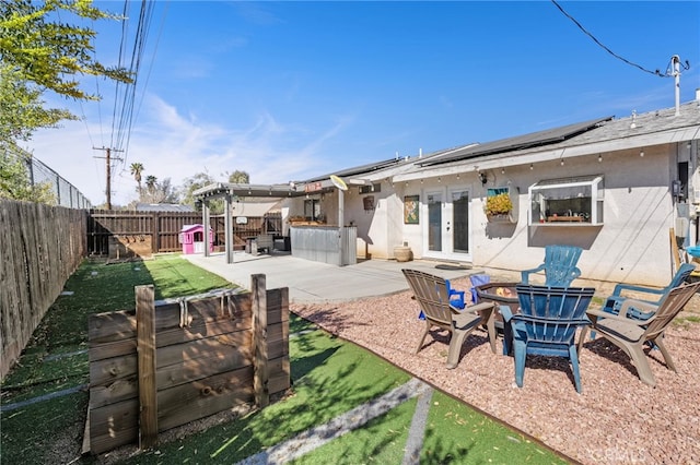 back of property with a fire pit, a fenced backyard, french doors, roof mounted solar panels, and stucco siding