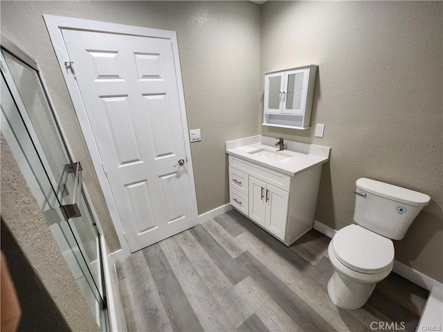 full bath featuring a shower with door, toilet, vanity, wood finished floors, and baseboards