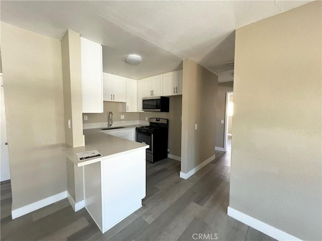 kitchen featuring appliances with stainless steel finishes, dark wood-type flooring, white cabinetry, a sink, and a peninsula