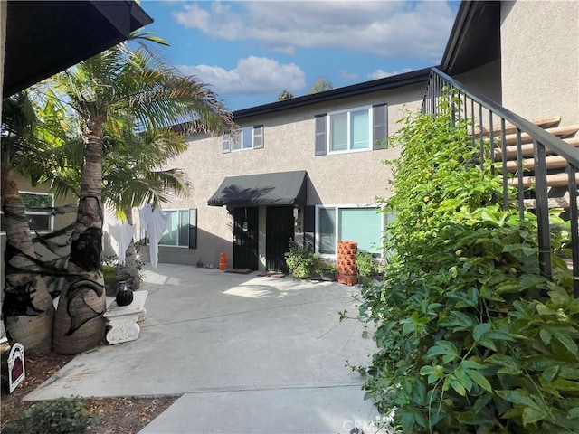 view of front of house with a patio, stairway, and stucco siding