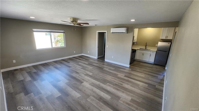 interior space with a textured ceiling, a sink, baseboards, a wall mounted AC, and dark wood finished floors