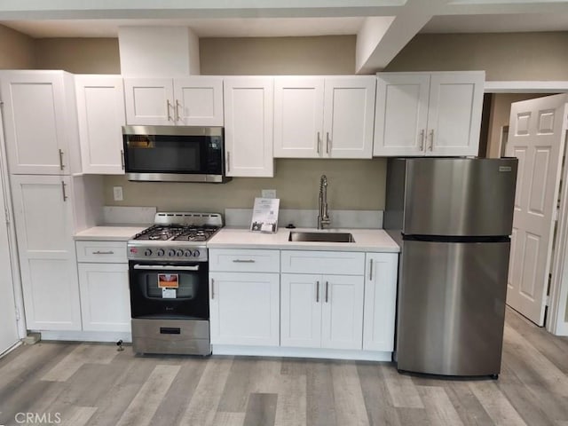 kitchen with stainless steel appliances, a sink, light countertops, and white cabinets