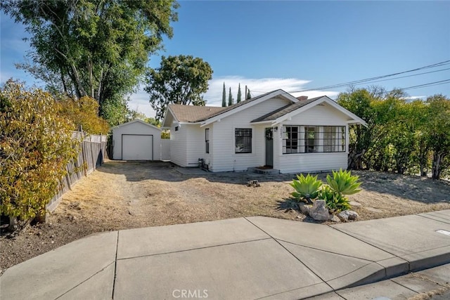 ranch-style home featuring driveway, a detached garage, fence, and an outdoor structure