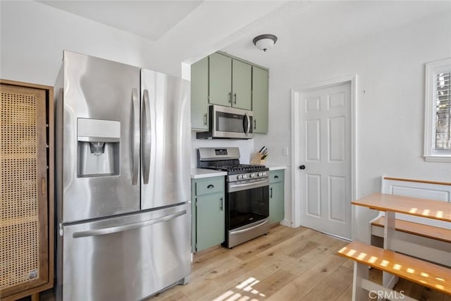 kitchen featuring appliances with stainless steel finishes, light wood-type flooring, light countertops, and green cabinetry