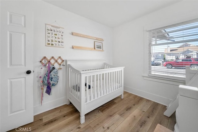 bedroom with a nursery area, baseboards, and wood finished floors