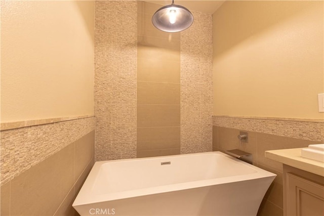full bathroom featuring a freestanding bath, vanity, tile walls, and wainscoting