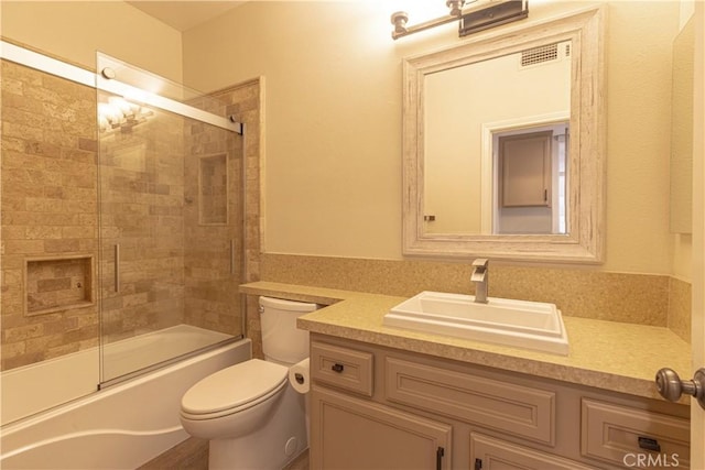 bathroom featuring toilet, vanity, shower / bath combination with glass door, and visible vents