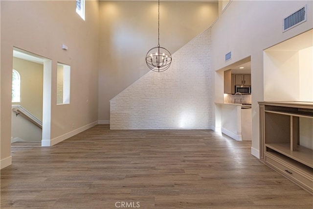 unfurnished living room featuring visible vents, a high ceiling, wood finished floors, and an inviting chandelier