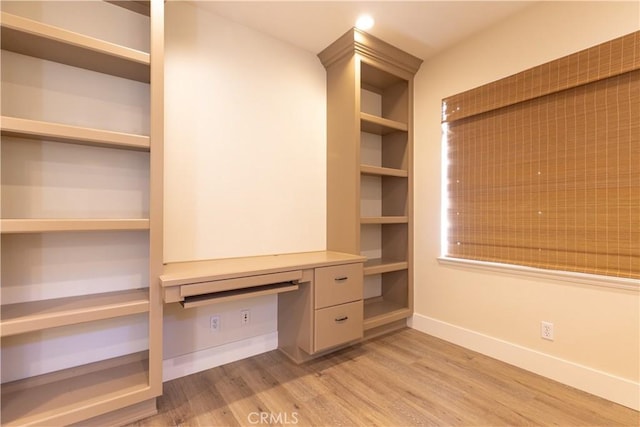 interior space featuring built in desk, baseboards, and light wood-style flooring