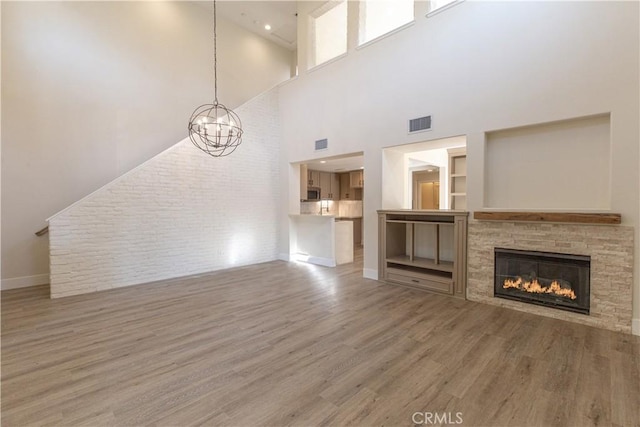 unfurnished living room featuring a chandelier, wood finished floors, a stone fireplace, baseboards, and visible vents