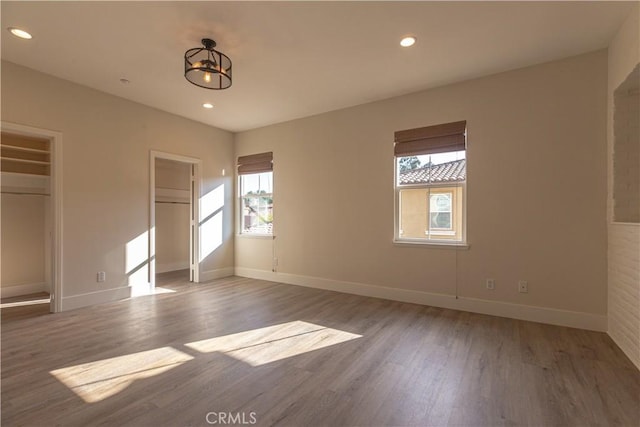 unfurnished bedroom featuring two closets, recessed lighting, baseboards, and wood finished floors