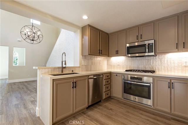 kitchen featuring a peninsula, stainless steel appliances, tasteful backsplash, a sink, and light wood-style floors