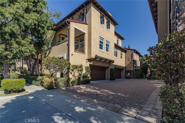 view of front of property with stucco siding, an attached garage, a balcony, and decorative driveway