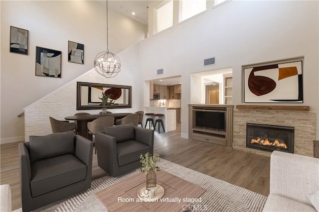 living room featuring baseboards, a chandelier, visible vents, a stone fireplace, and wood finished floors