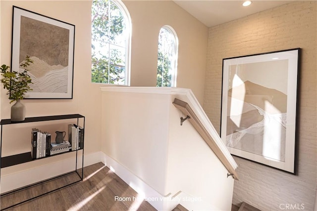 stairs featuring wood finished floors, recessed lighting, and brick wall