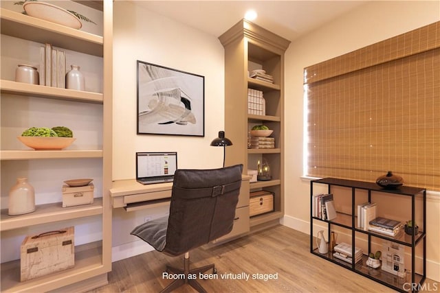 office space with built in study area, baseboards, built in shelves, and wood finished floors