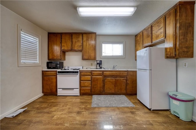 kitchen with light countertops, white appliances, a sink, and brown cabinets