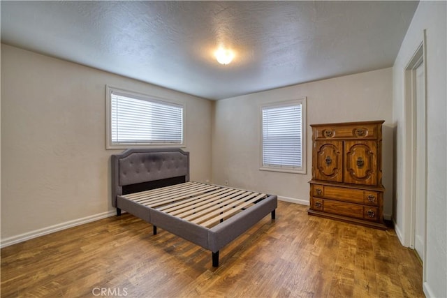 bedroom with multiple windows, baseboards, and wood finished floors