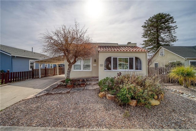 view of front of property featuring a tile roof, fence, driveway, stucco siding, and a carport