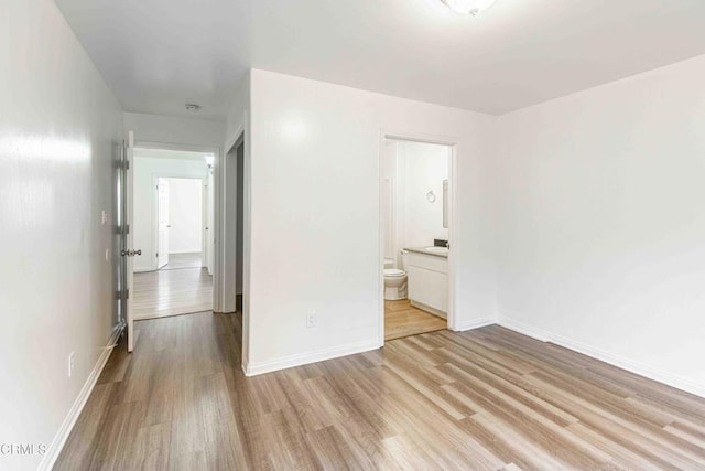 unfurnished bedroom with light wood-style floors, baseboards, and ensuite bathroom