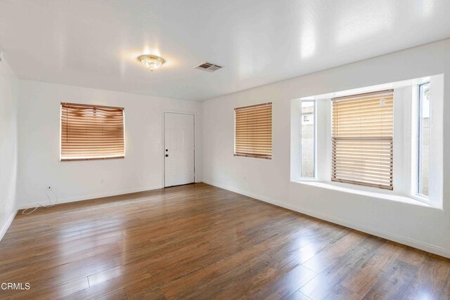 empty room with a wealth of natural light, wood finished floors, and visible vents