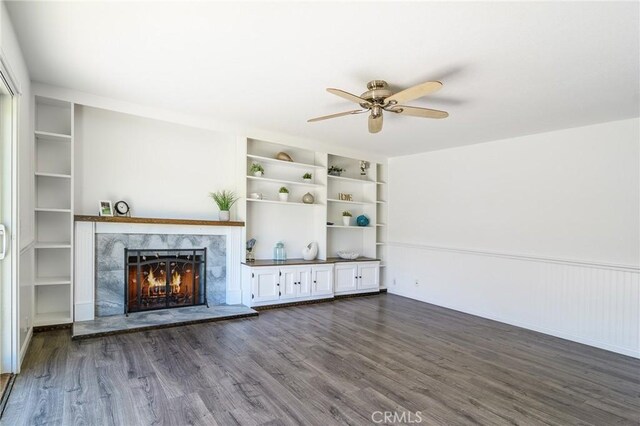 unfurnished living room featuring ceiling fan, dark wood finished floors, built in shelves, and a premium fireplace