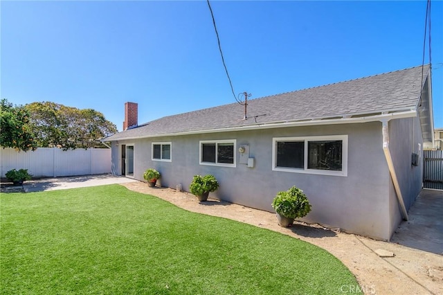 back of house with a yard, fence, a shingled roof, and stucco siding