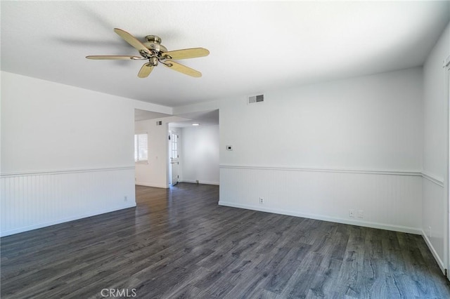 spare room with dark wood-style floors, a wainscoted wall, visible vents, and a ceiling fan