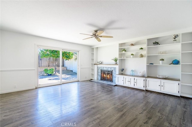 unfurnished living room with dark wood-style floors, built in shelves, a high end fireplace, and a ceiling fan