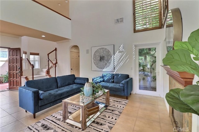 living area featuring light tile patterned floors, visible vents, arched walkways, and stairs