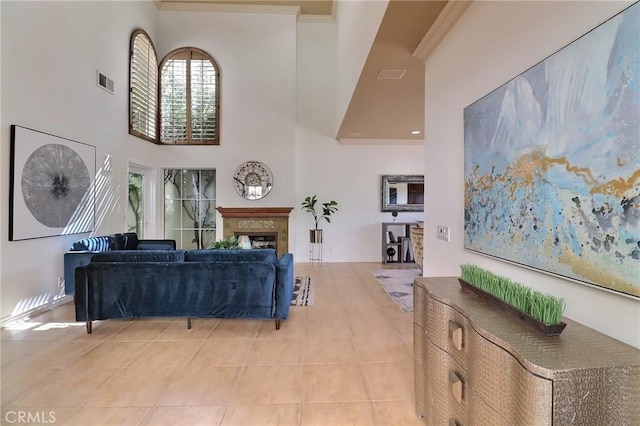 living room featuring visible vents, light tile patterned flooring, a fireplace, ornamental molding, and a towering ceiling