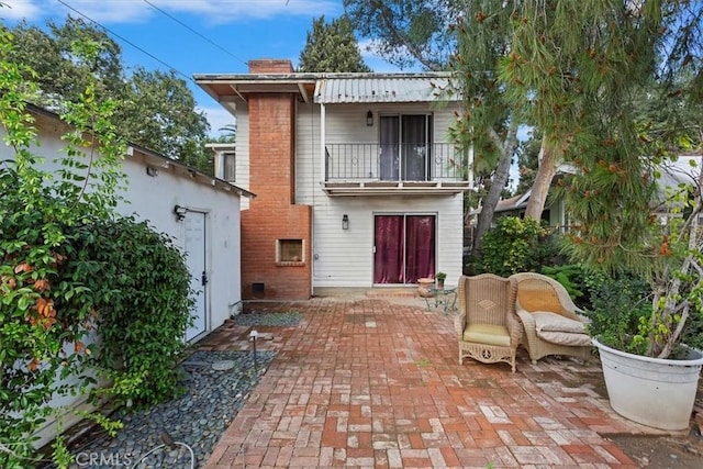 back of property featuring a patio, a chimney, and a balcony