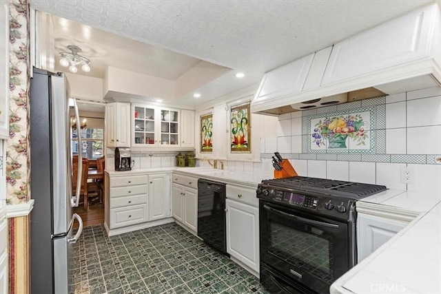 kitchen with black appliances, tasteful backsplash, white cabinetry, and light countertops