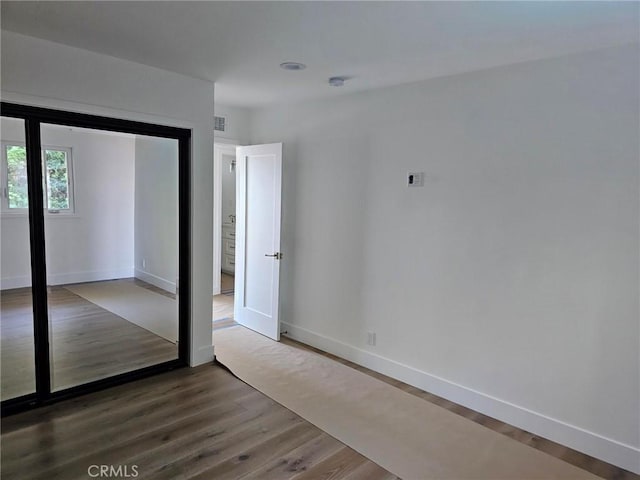 spare room with wood finished floors, visible vents, and baseboards