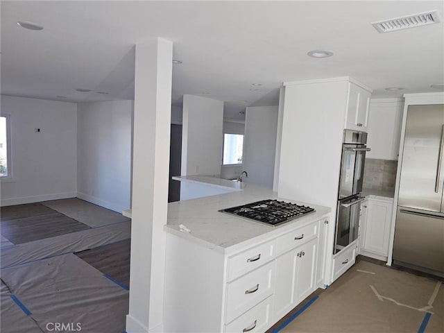 kitchen featuring stainless steel appliances, visible vents, backsplash, open floor plan, and a peninsula