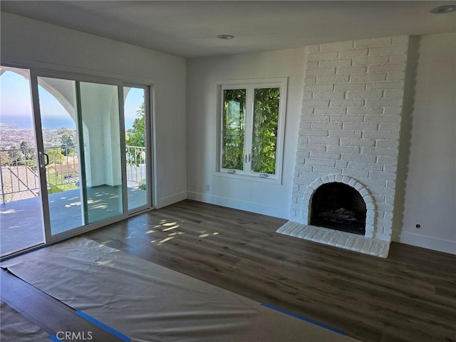 unfurnished living room with dark wood-type flooring, a brick fireplace, a healthy amount of sunlight, and baseboards