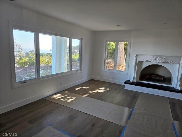 unfurnished living room featuring a fireplace with raised hearth, a wealth of natural light, hardwood / wood-style flooring, and baseboards