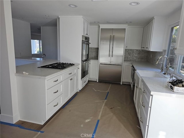 kitchen featuring stainless steel appliances, decorative backsplash, white cabinetry, a sink, and light stone countertops