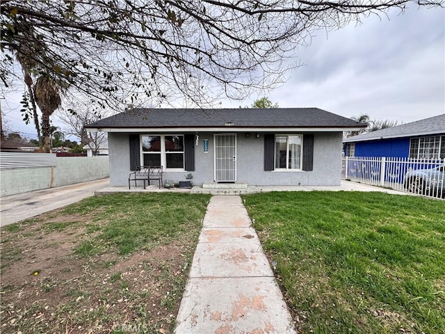 view of front of house with stucco siding, a shingled roof, a front lawn, and fence