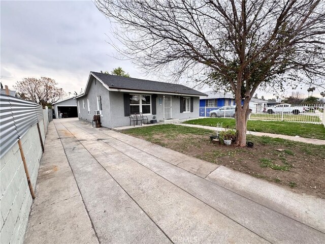 view of front of property with stucco siding, fence, roof with shingles, an outdoor structure, and a front yard