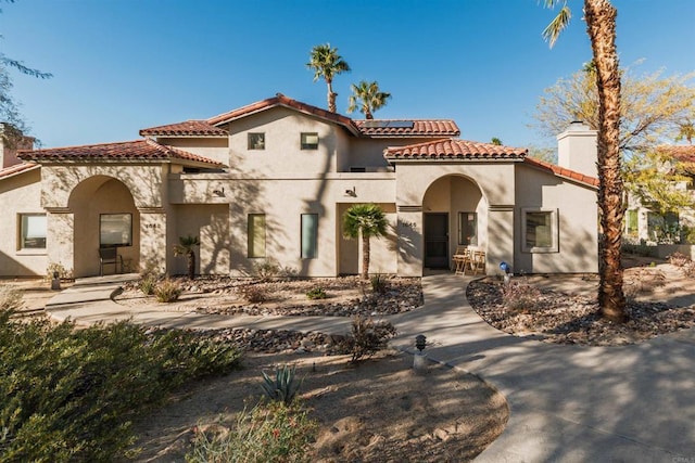 mediterranean / spanish house with a tiled roof, roof mounted solar panels, a chimney, and stucco siding