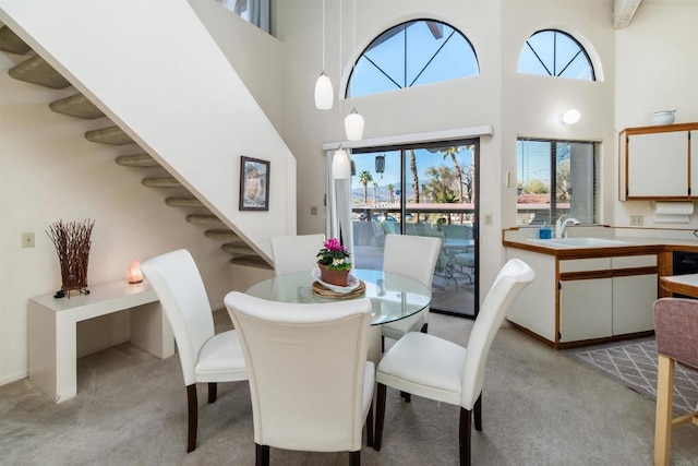 dining area featuring light carpet, stairway, and a towering ceiling