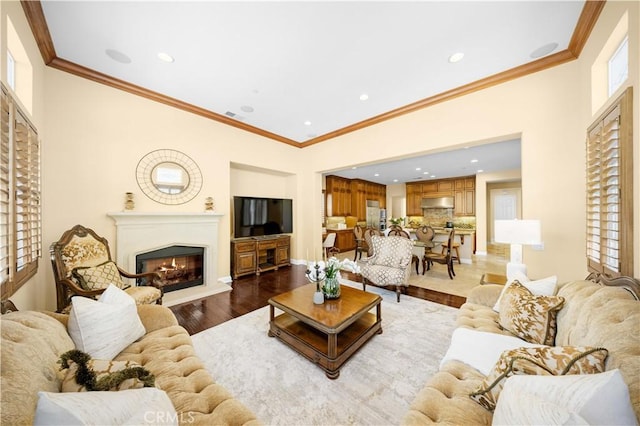 living area with a glass covered fireplace, wood finished floors, recessed lighting, and crown molding