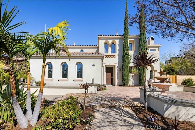 mediterranean / spanish-style home with stucco siding, a tiled roof, and fence